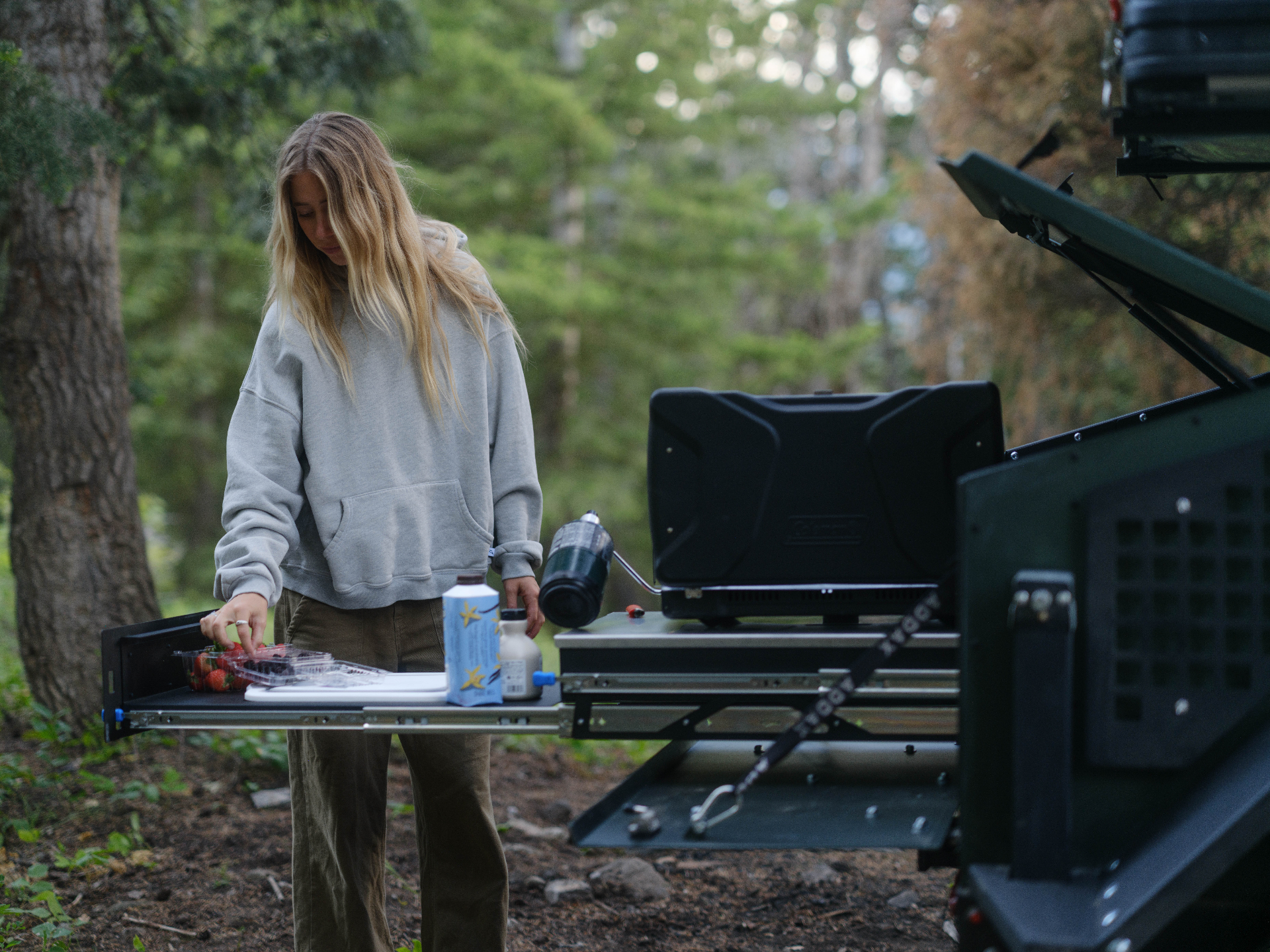 Camper preparing food on the ADDAX slide-out kitchen at a forest campsite