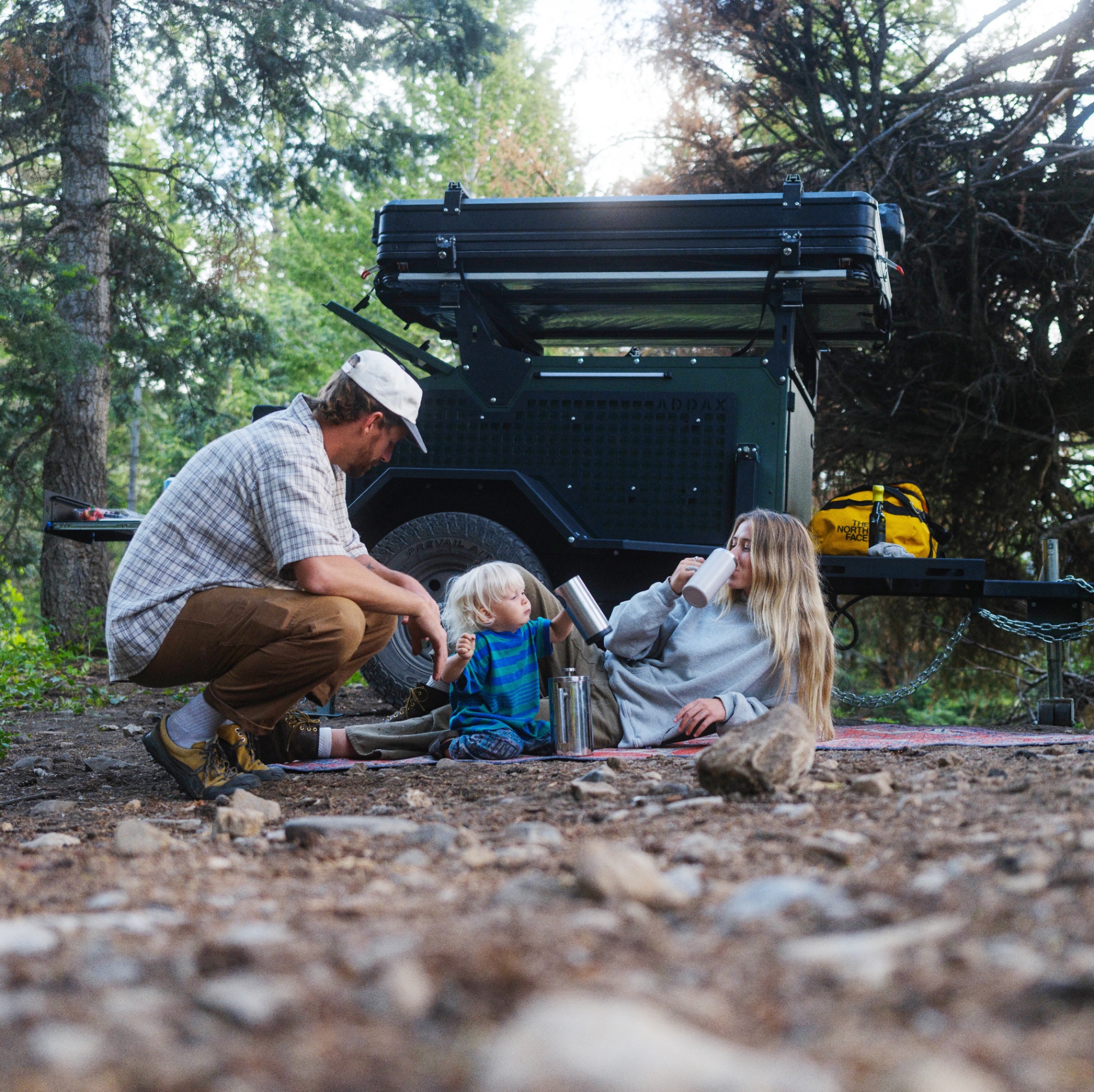 Family relaxing at camp with their ADDAX trailer in the woods