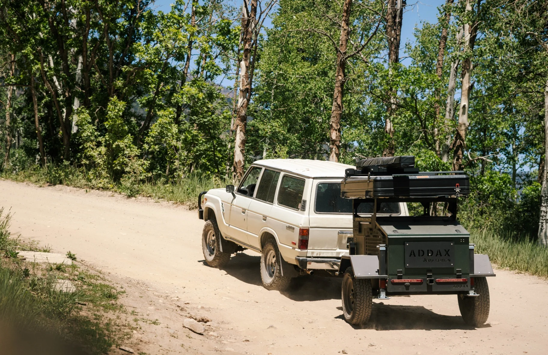 ADDAX Basecamp trailer hitched behind an overland rig on a backcountry road